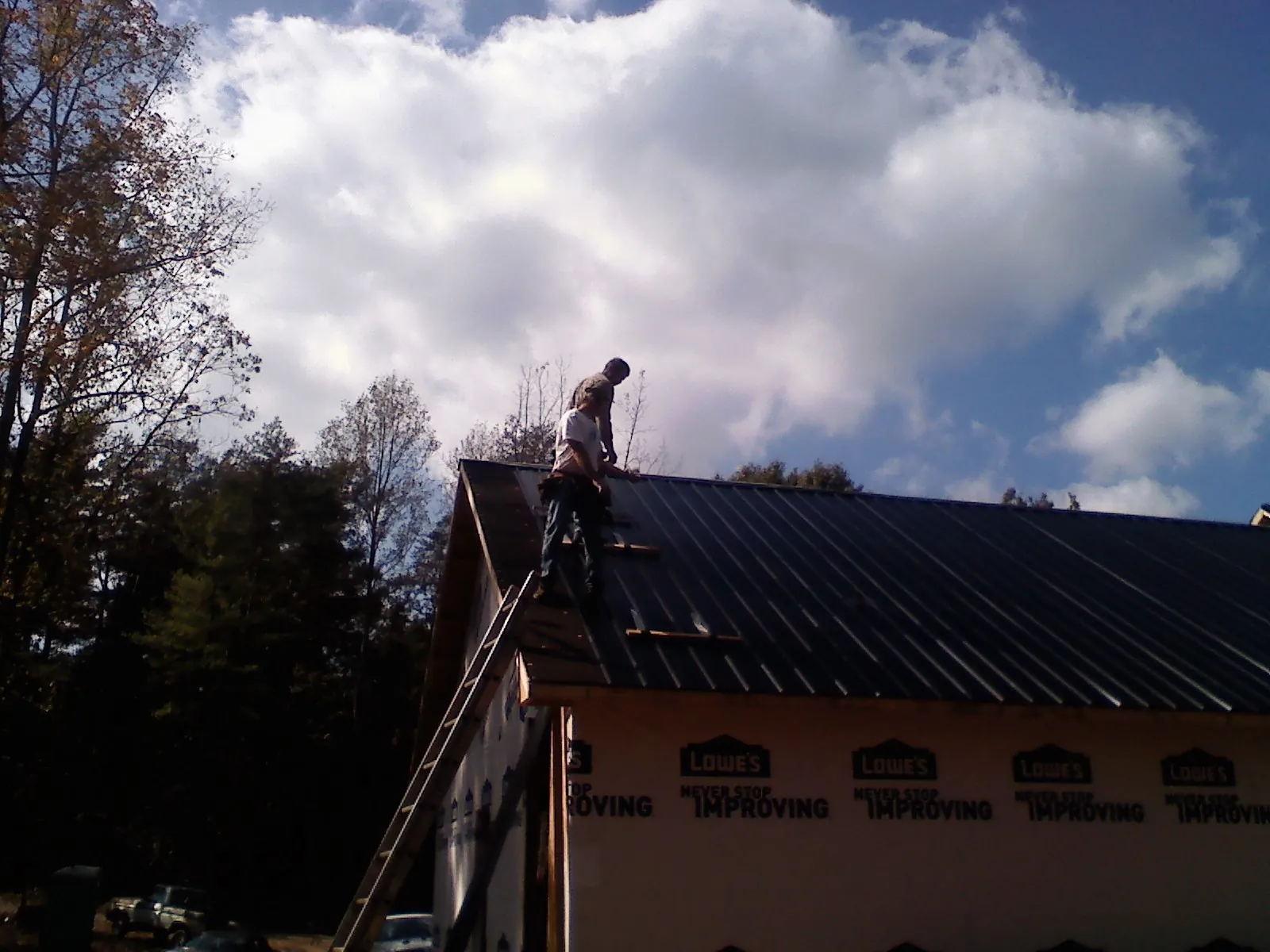 Roofer fastening dark metal panels high against a cloudy sky, from a Roof Inspection job in Spring Grove