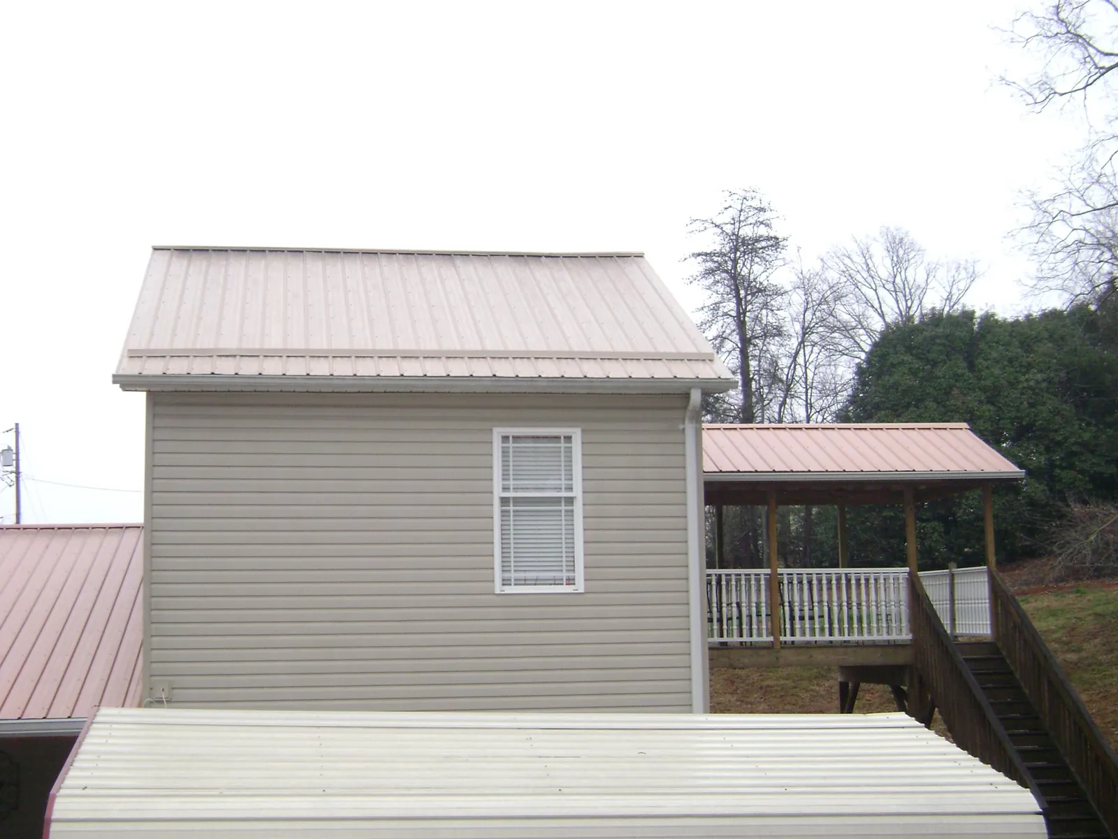 Tan metal roofs on a two story addition and attached porch, from a Roof Replacement job in Spring Grove